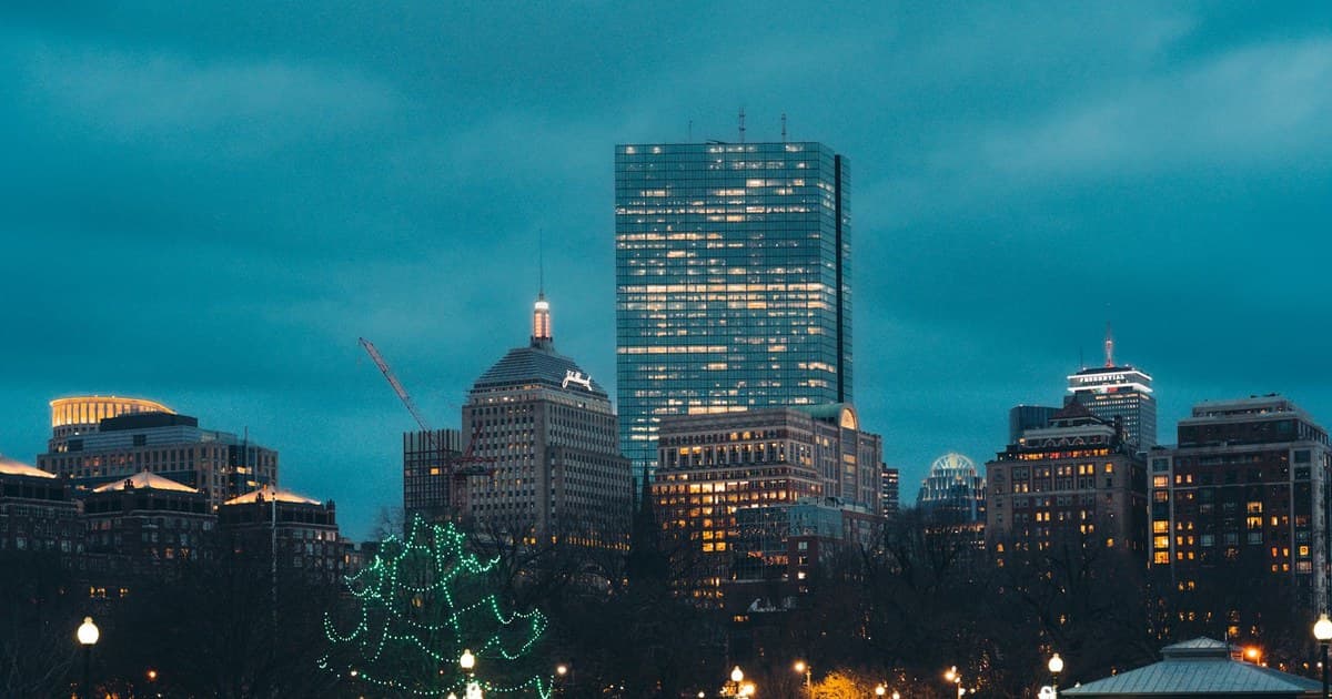 Evening view of Boston's skyline with festive Christmas tree lights in a city park.